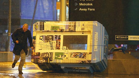 A programme stand is stricken on its side as a supporter runs through the wind and driving rain at the Etihad.