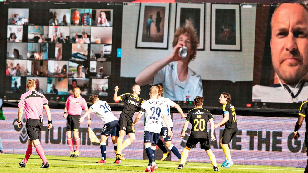 Players vie for the ball as fans are streamed live on to the screens on the sidelines during a match in Denmark.