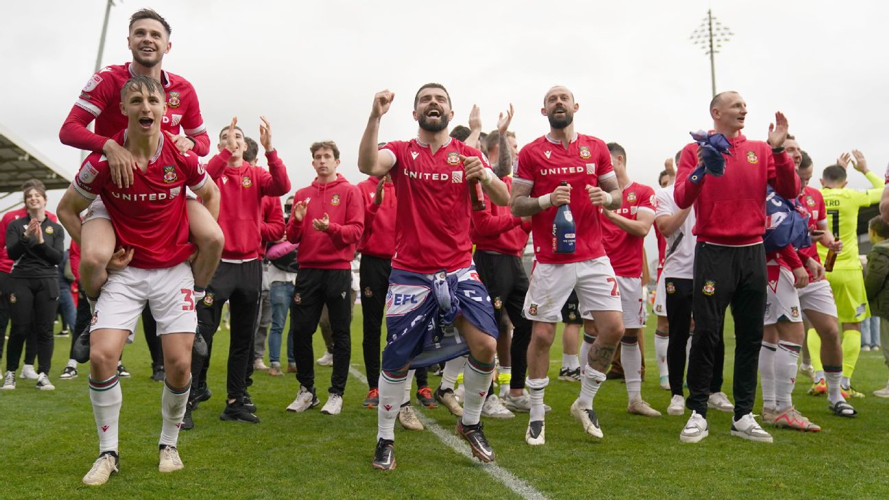 Wrexham players on the pitch celebrating promotion to League One after the final whistle of the Sky Bet League Two match at the SToK Cae Ras [1296x729]